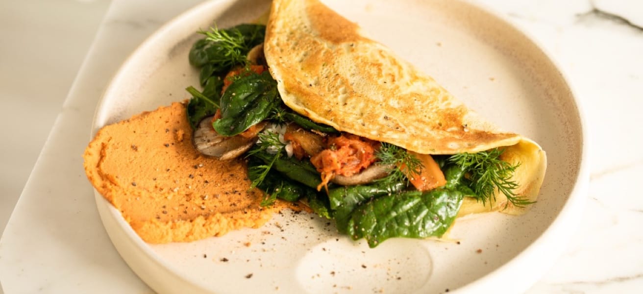 omelette filled with green leaves, served on a white plate alongside a portion of mashed potatoes.